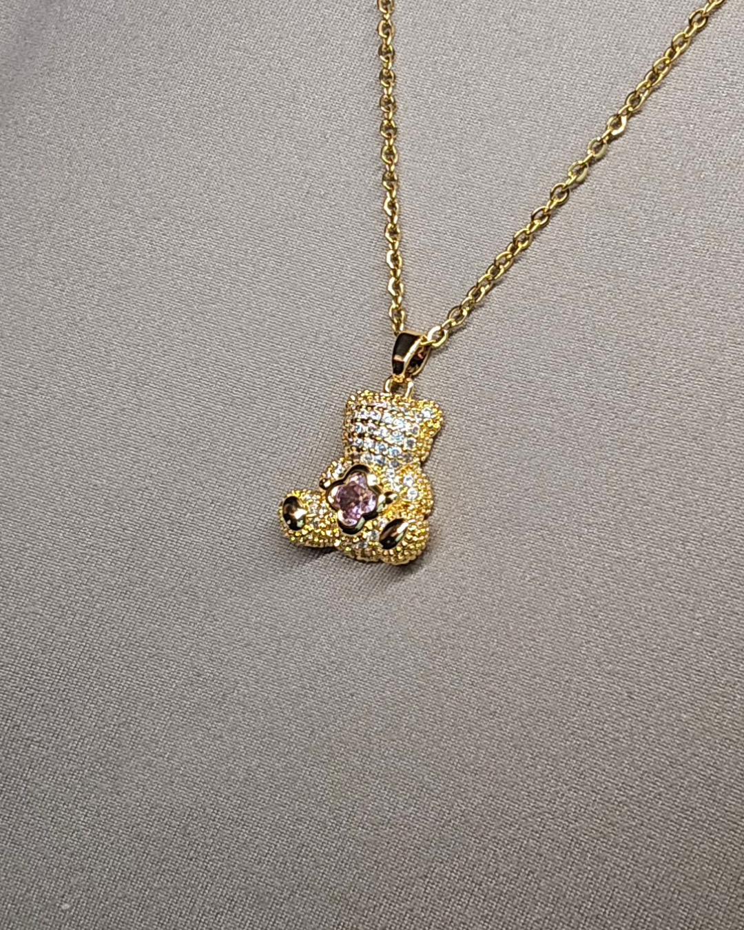 Gold teddy bear pendant necklace on a gray background