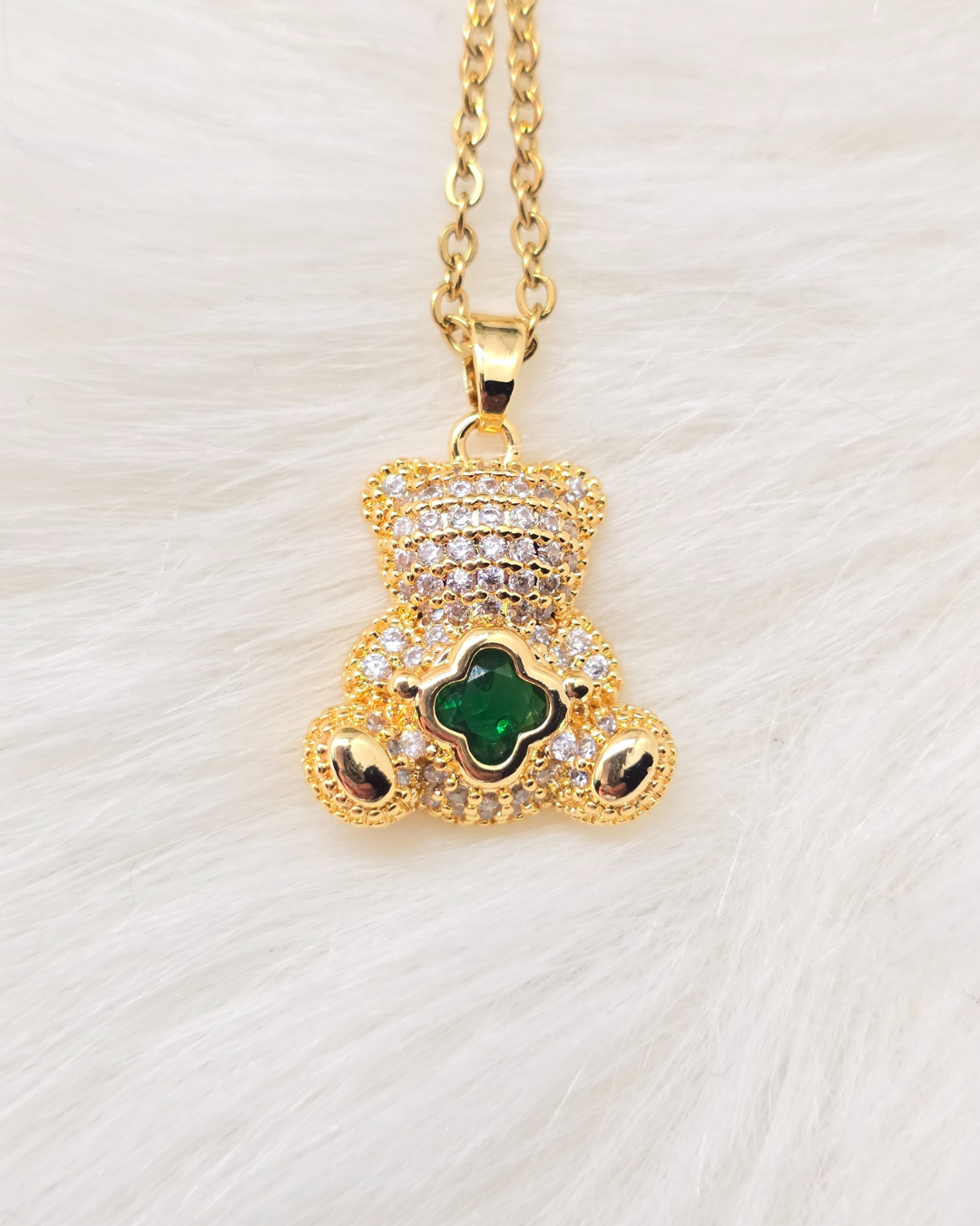 Gold teddy bear pendant with green gemstone on a white background