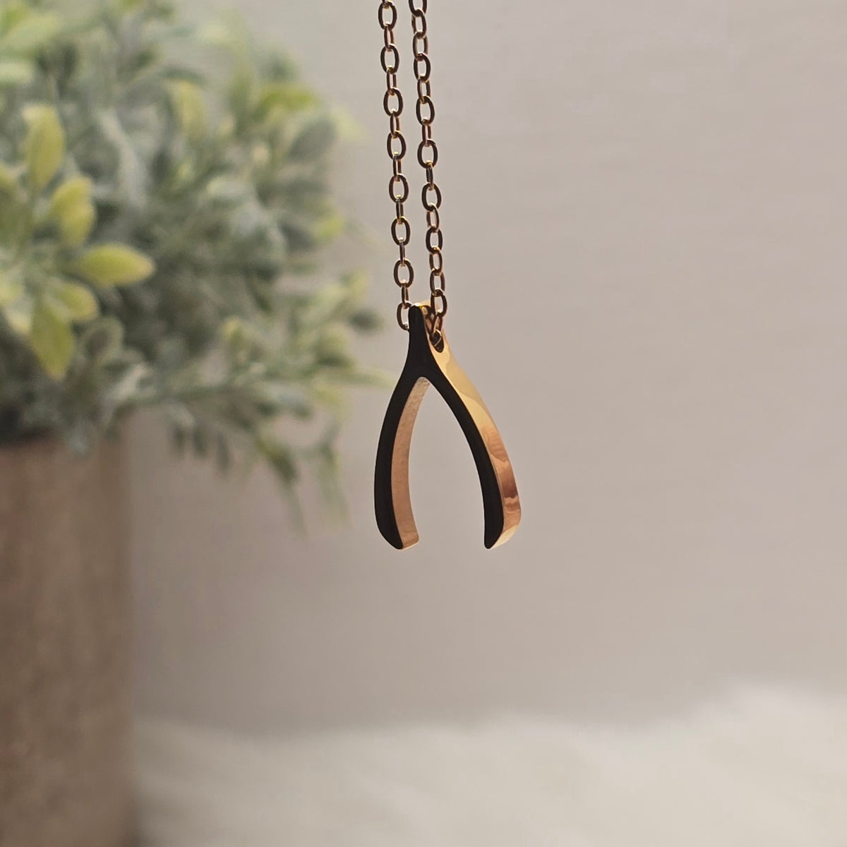 Gold wishbone pendant necklace with a plant in the background