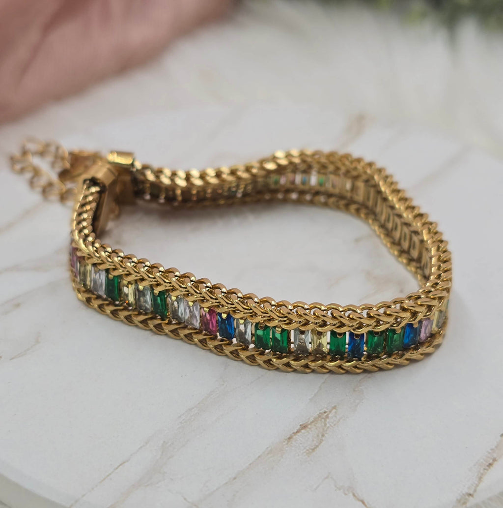 Gold bracelet with colorful gemstones on a marble surface
