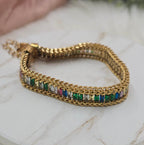 Gold bracelet with colorful gemstones on a marble surface