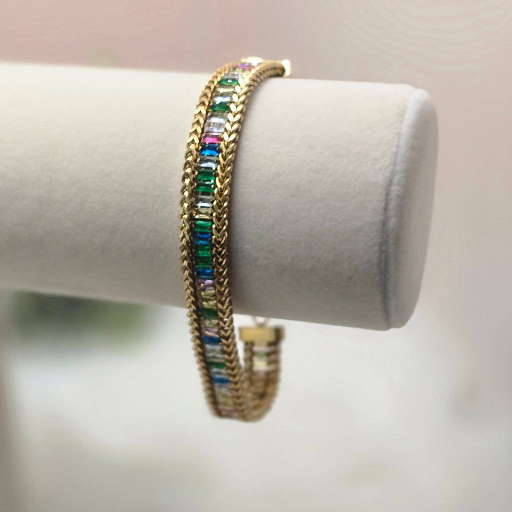 Gold bracelet with colorful stones on a white cylindrical stand