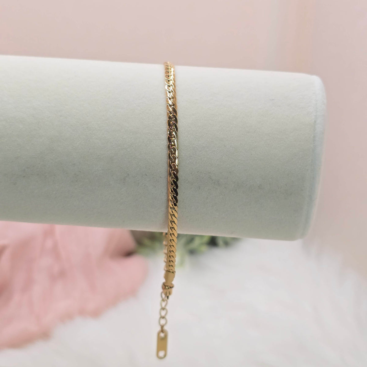 Gold chain bracelet on a white cylindrical stand with a blurred background