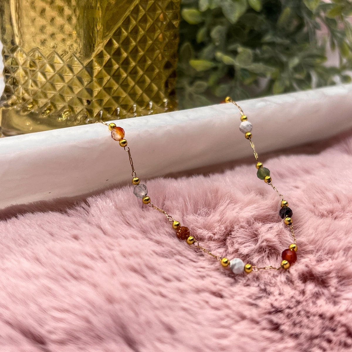 Gemma Dainty Necklace with multicolored beads and a gold-tone chain on pink fabric.