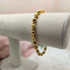 Gold beaded bracelet on a white stand with a pink background