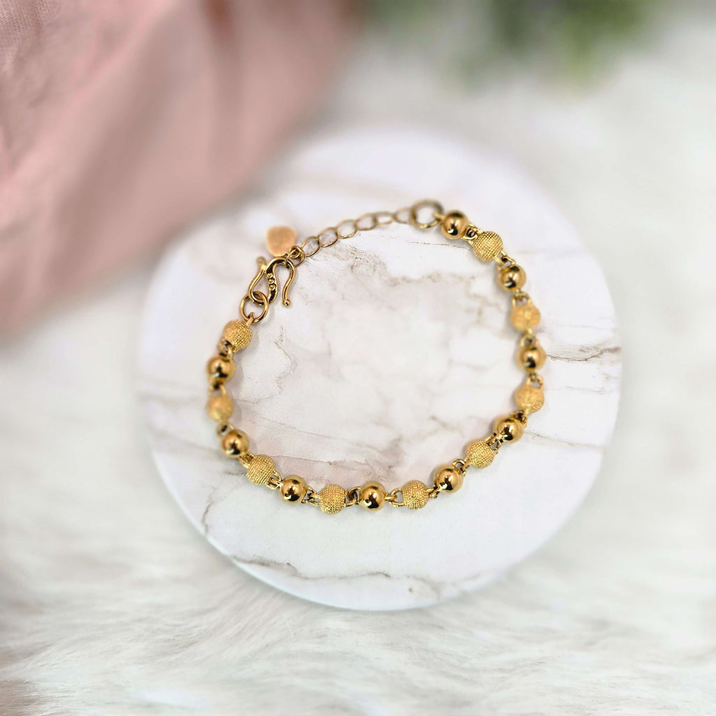 Gold beaded bracelet on a white marble surface